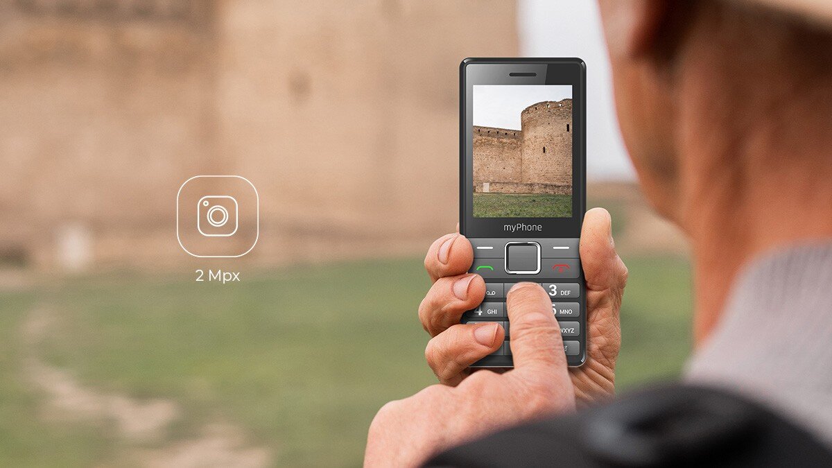 Mężczyzna robi zdjęcie zamku telefonem myPhone 7340 LTE; na ekranie widok murów; obok ikona aparatu 2 Mpx.