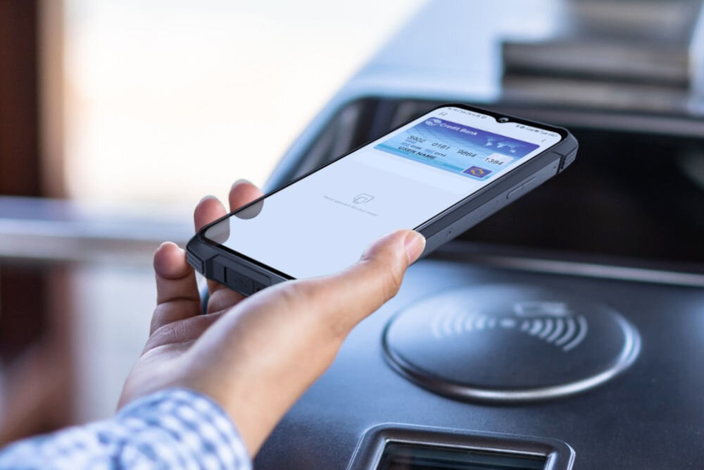 Smartfon CUBOT King Kong 11 5G 16/256GB 6.72 120Hz Czarny Ręka trzyma smartfon Cubot, używając go do zbliżeniowej płatności (NFC) na terminalu, z widoczną wirtualną kartą debetową na ekranie