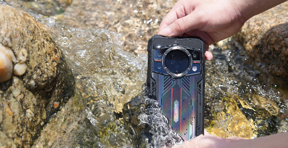 Smartfon CUBOT King Kong 11 5G 16/256GB 6.72 120Hz Czarny Ręce trzymające pancerny smartfon Cubot pod strumieniem wody w strumieniu lub rzece, z widoczną tylną obudową i okrągłym wyświetlaczem pomocniczym, ilustrujące wodoodporność