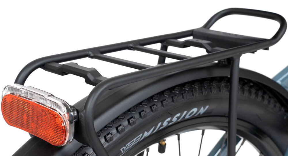 Zdjęcie przedstawia tylną część roweru z bagażnikiem i czerwonym odblaskiem. Na oponie widoczny jest napis \'MISSION\'.