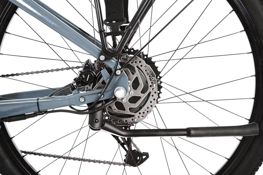Zbliżenie na tylne koło roweru z widocznym mechanizmem hamulcowym tarczowym i częścią ramy w kolorze szarym.