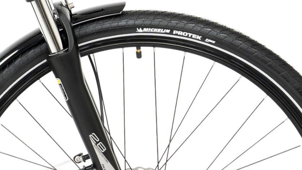 Zbliżenie na przednie koło roweru z widoczną oponą Michelin Protek. Na widelcu znajduje się napis \'28\'.