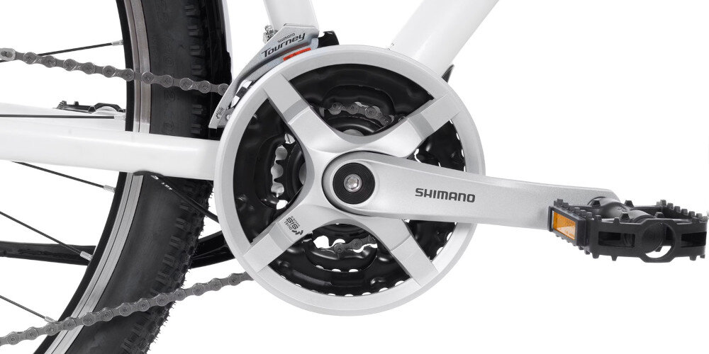 Zbliżenie na mechanizm korbowy roweru z widocznym napisem \'SHIMANO\' na ramieniu korby. Obok znajduje się napis \'Tourney\' na przerzutce.