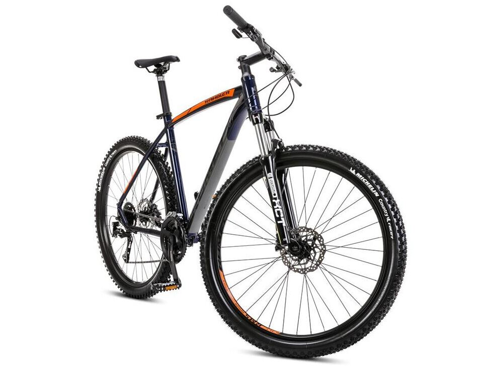 Rower górski MTB w kolorze granatowo-pomarańczowym z dużymi kołami i amortyzowanym widelcem. Na ramie widoczny jest napis \'Rambler\'.