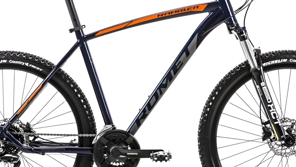 Rower górski w kolorze granatowo-pomarańczowym z widocznym napisem \'ROMET\' na ramie. Na widelcu znajduje się napis \'RCT\' oraz logo \'SHIMANO\' na mechanizmie korbowym.