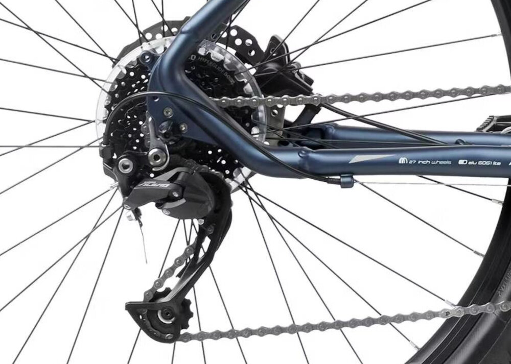 Zdjęcie przedstawia tylne koło roweru z widocznym mechanizmem przerzutki i tarczą hamulcową. Na ramie widoczny jest napis: \'27 inch wheels\' oraz \'alu 6061 t6\'.