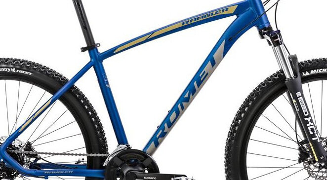 Rower górski MTB w kolorze niebiesko-żółtym z widocznym logo \'ROMET\' na ramie. Opony mają wyraźny bieżnik, a rower wyposażony jest w amortyzowany widelec.