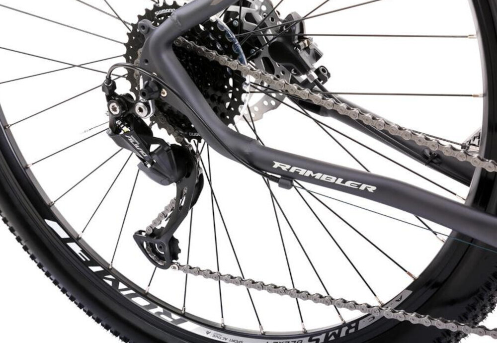 Zbliżenie na tylne koło roweru górskiego z widocznym mechanizmem przerzutki i łańcuchem. Na ramie widoczny napis \'RAMBLER\'.