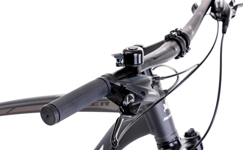 Zbliżenie na kierownicę roweru z widocznym dzwonkiem i manetką Shimano. Na ramie roweru widoczny jest napis \'ROMET\'.