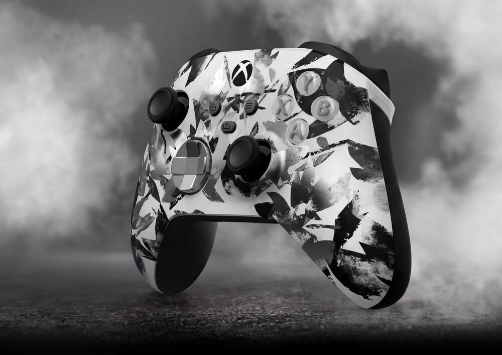 Kontroler do gier z czarno-białym wzorem kamuflażu, z widocznym logo Xbox na górze. Tło jest szare i zamglone.