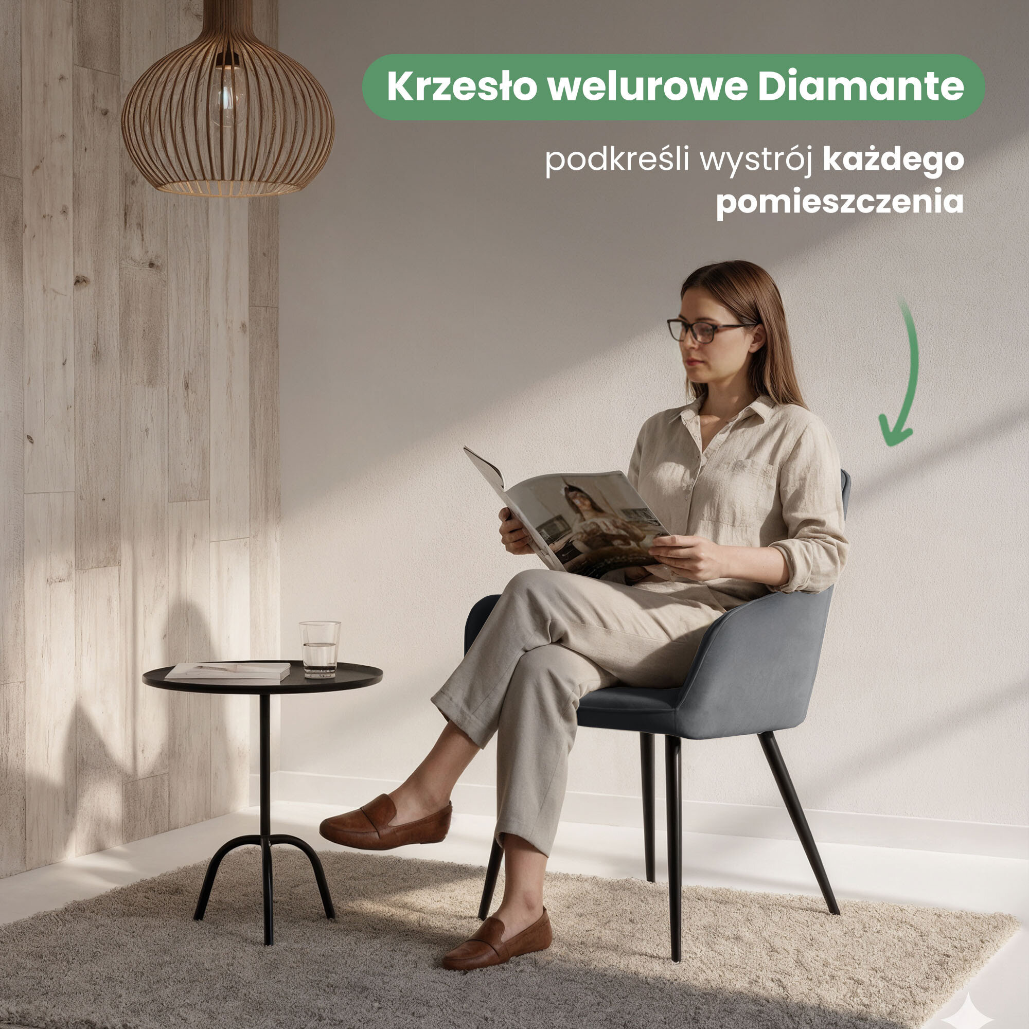 Osoba siedzi na ciemnoszarym, welurowym krześle z czarnymi nogami, obok znajduje się mały stolik z szklanką i czasopismem. Na obrazie widoczny jest tekst: \'Krzesło welurowe Diamante podkreśli wystrój każdego pomieszczenia\'.