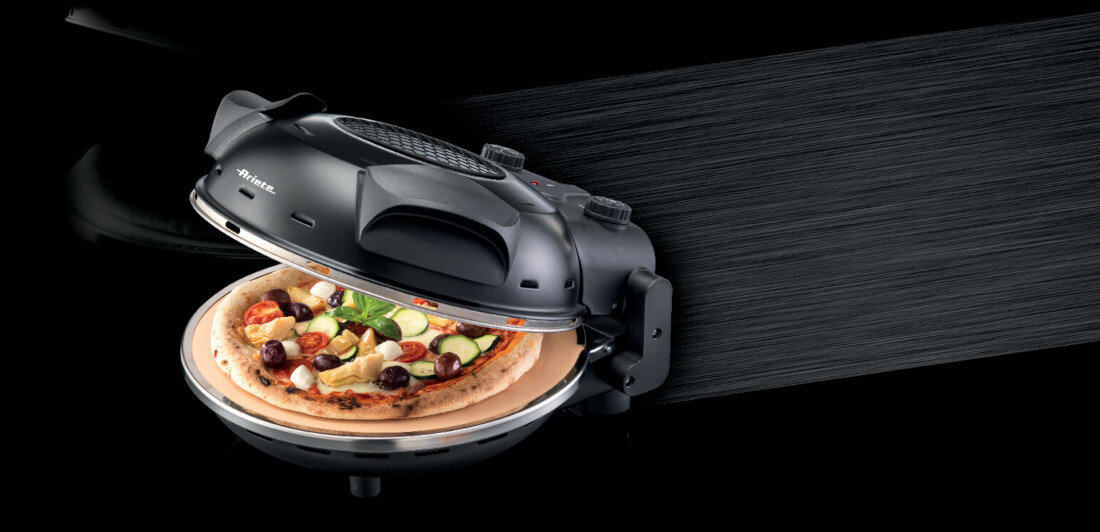 Czarny piec do pizzy z otwartą pokrywą, w środku znajduje się pizza z różnymi składnikami. Na urządzeniu widoczne jest logo \'Ariete\'.