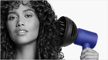 Modelka z kręconymi włosami przykłada suszarkę z dyfuzorem w trybie rozpraszania do włosów.