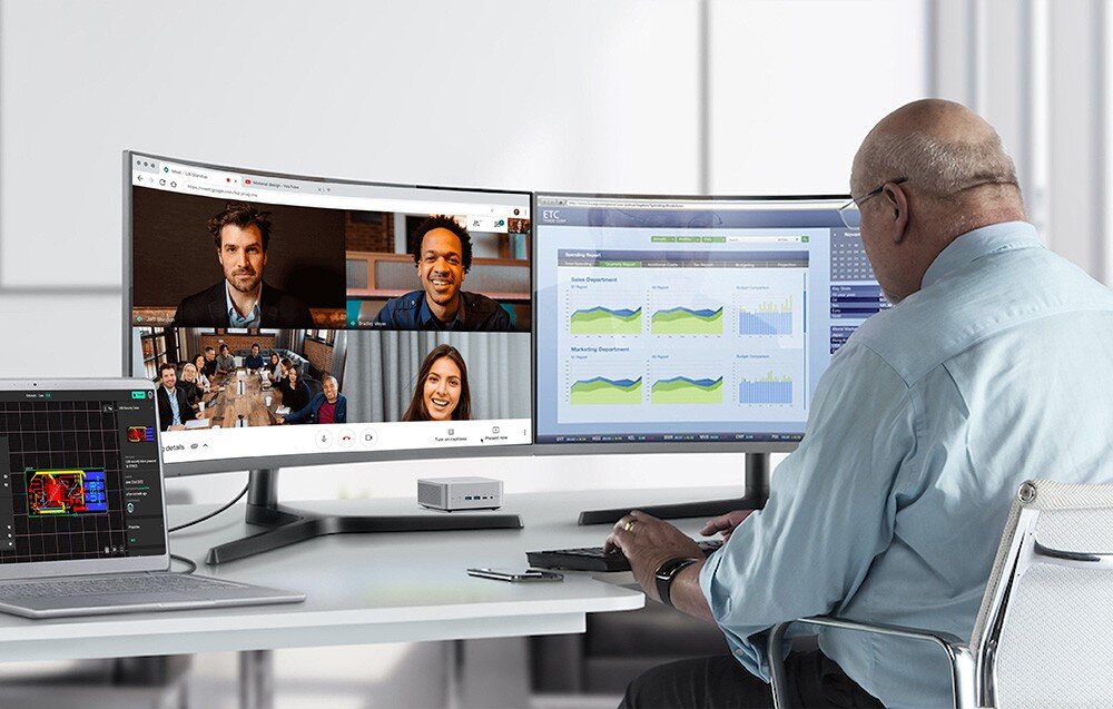 Komputer MINISFORUM X1-255 Mężczyzna pracuje przy biurku z dwoma monitorami wyświetlającymi wideokonferencję i wykresy, a mały komputer stoi pod ekranami