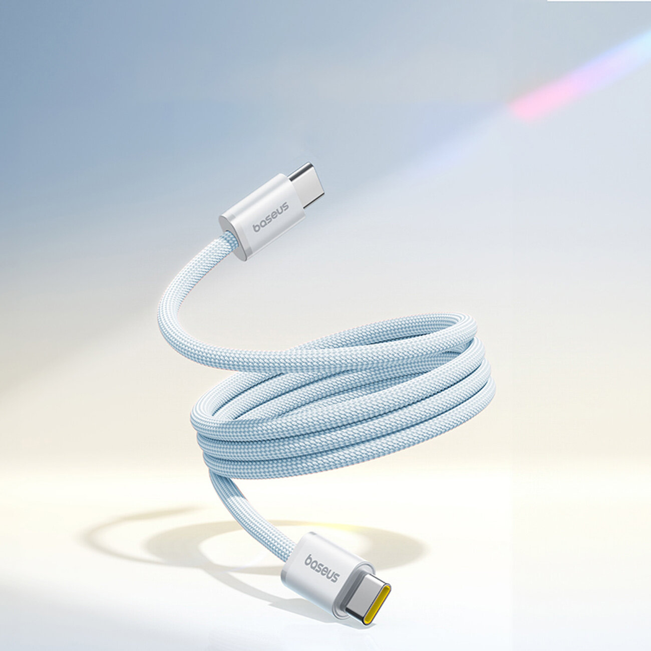 Na obrazie widoczny jest kabel USB C w oplocie, z końcówkami oznaczonymi logo \'baseus\'. Kabel jest w kolorze jasnoniebieskim i unosi się w powietrzu na jasnym tle.