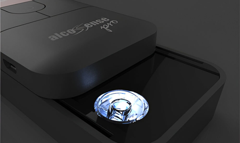 Na obrazie widoczny jest alkomat z napisem \'alcoSense pro\' na obudowie. Urządzenie ma ciemną obudowę i podświetlany element na powierzchni.