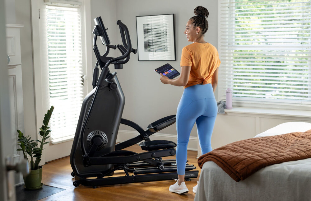 Orbitrek eliptyczny SCHWINN 590E 18kg 51cm osoba stoi obok urządzenia w pomieszczeniu 25 poziomów oporu  dostosowanie intensywność treningu do swoich potrzeb automatyczny system oporu ECB płyna cicha praca