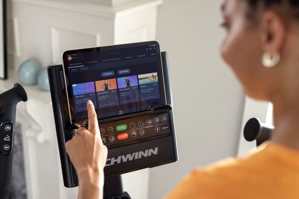 Orbitrek eliptyczny SCHWINN 590E 18kg 51cm osoba dotyka tableta z włączoną aplikacją moduł Bluetooth BLE 4.0 synchronizacja z aplikacją JRNY lub innymi platformami fitness 13 wgranych programów dostęp do ponad 1000 treningów w aplikacji JRNY aplikacja dostępna na systemy Android i iOS