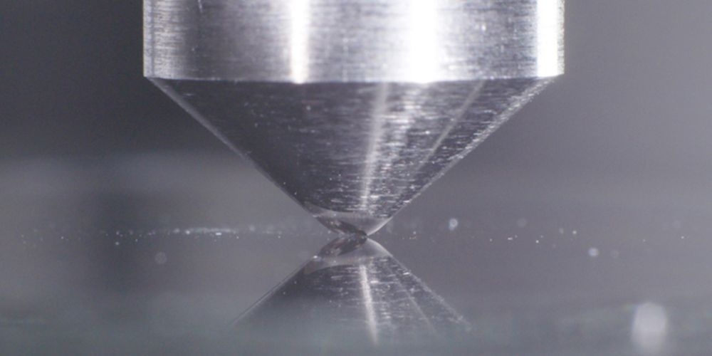 Zbliżenie na test wytrzymałości szkła – stalowy stożek naciskający na powierzchnię, ilustracja odporności ekranu laptopa ASUS Zenbook 14 z powłoką Corning Gorilla Glass. 