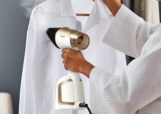 Osoba trzyma w ręce parownicę DT9820 AeroSteam i prasuje białą koszulę.