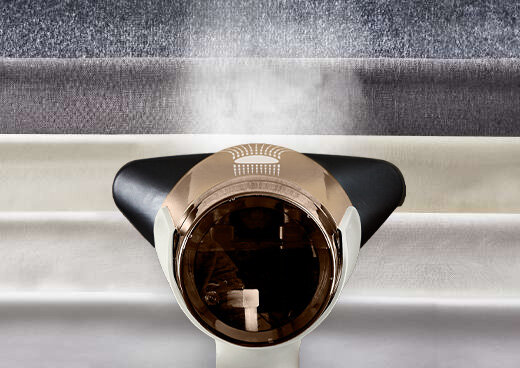 Zbliżenie na głowicę parownicy DT9820 AeroSteam, która generuje strumień pary. W tle różne tkaniny.