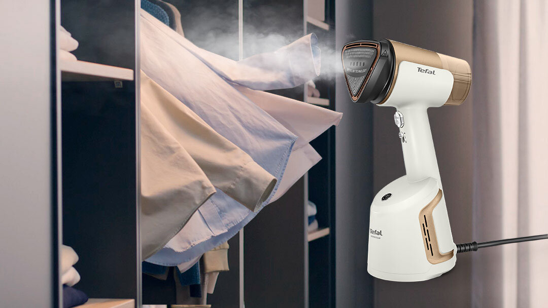 Parownica do ubrań TEFAL DT9820 przy szafie z wystającymi ubraniami. Parownica generuje strumień pary.