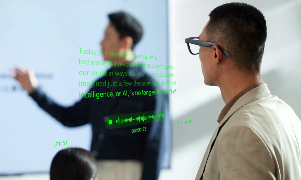 Osoba nosi okulary z wyświetlaczem, na którym widoczny jest tekst: \'Today, we stand at the cusp of a technological revolution that is reshaping our world in ways we could have scarcely imagined just a few decades ago. Artificial Intelligence, or AI, is no longer the stuff of\'. W tle znajduje się inna osoba, która wydaje się prezentować coś na ekranie.