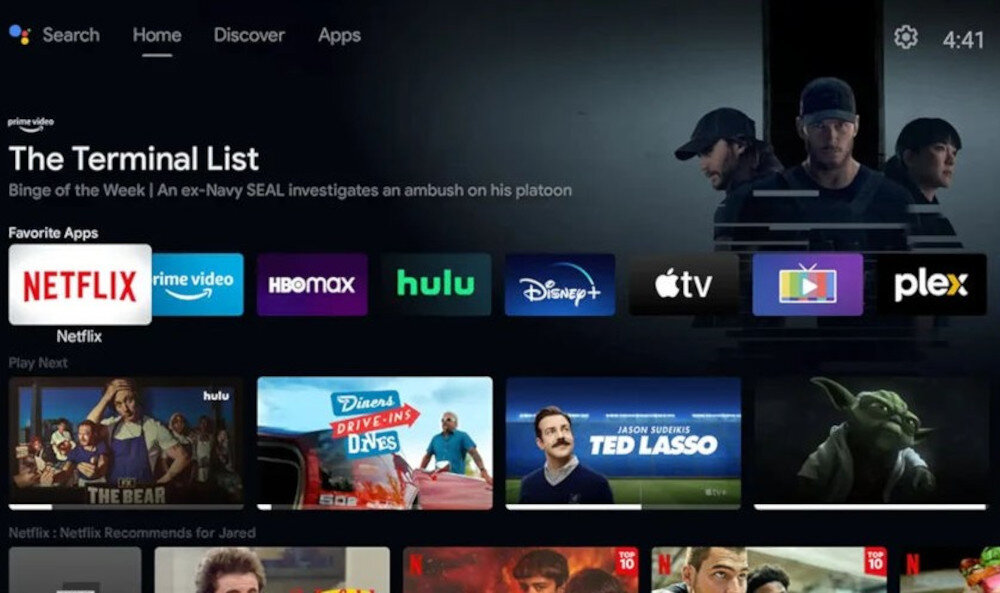 Interfejs użytkownika z aplikacjami streamingowymi, takimi jak Netflix, Prime Video, HBO Max, Hulu, Disney+, Apple TV i Plex. Na górze widoczny jest tytuł \'The Terminal List\' z krótkim opisem fabuły oraz zegar pokazujący godzinę 4:41.
