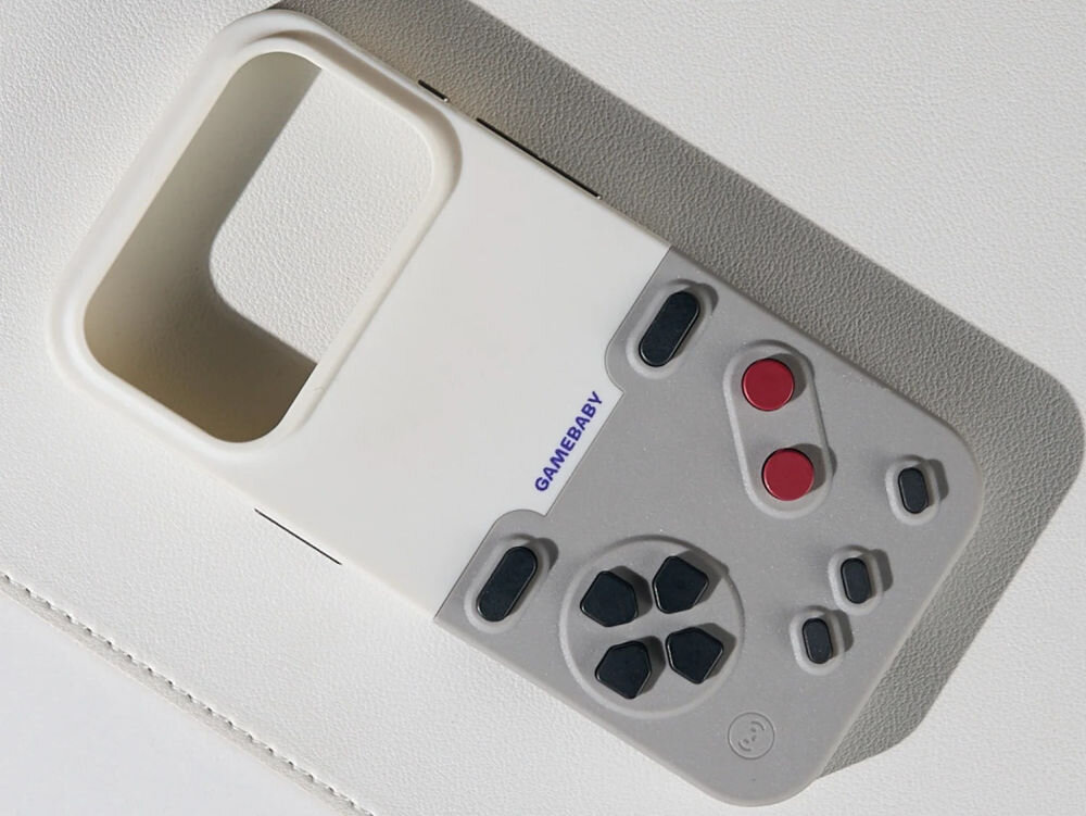 GameBaby retro gry na iPhone Zbliżenie na detale etui GameBaby: szary moduł kontrolera z czerwonymi przyciskami i czarnym d-padem na jasnym tle.