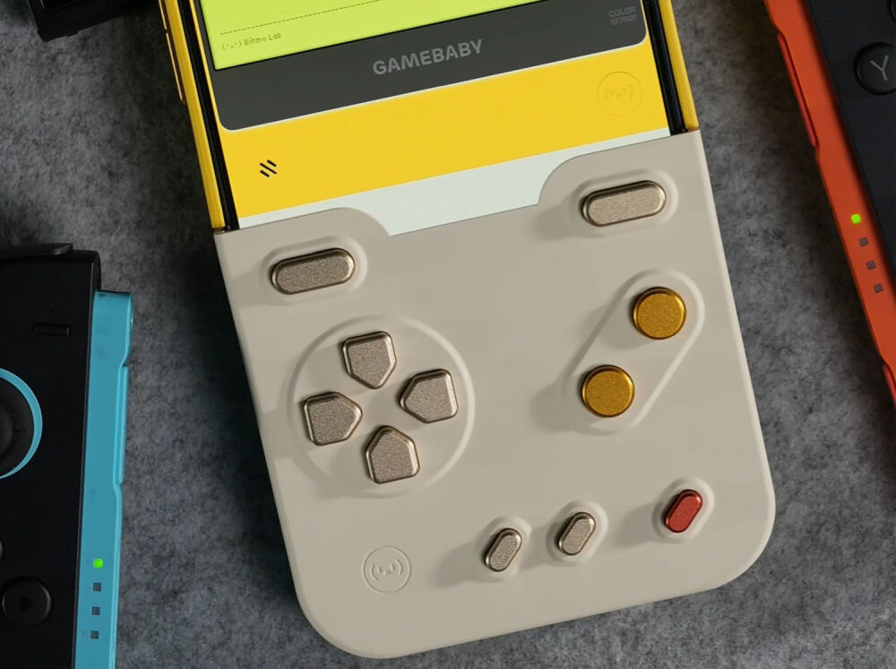 GameBaby fizyczne przyciski kontrolera Zbliżenie na panel kontrolny GameBaby z d-padem i złotymi przyciskami, zamontowany na smartfonie obok konsoli Nintendo Switch.