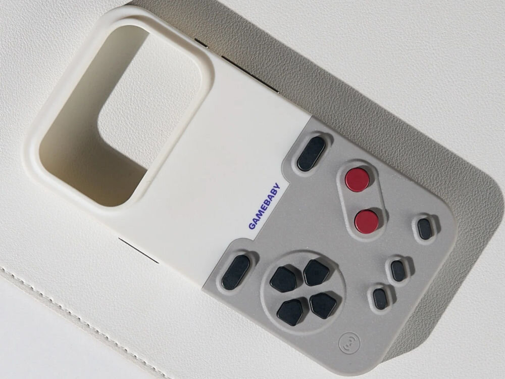 GameBaby retro gry na iPhone Zbliżenie na dwuczęściowe etui ochronne GameBaby leżące na jasnej powierzchni. Akcesorium posiada białą górną ramkę oraz szary panel z przyciskami w stylu retro, nawiązujący wyglądem do klasycznych konsol przenośnych.