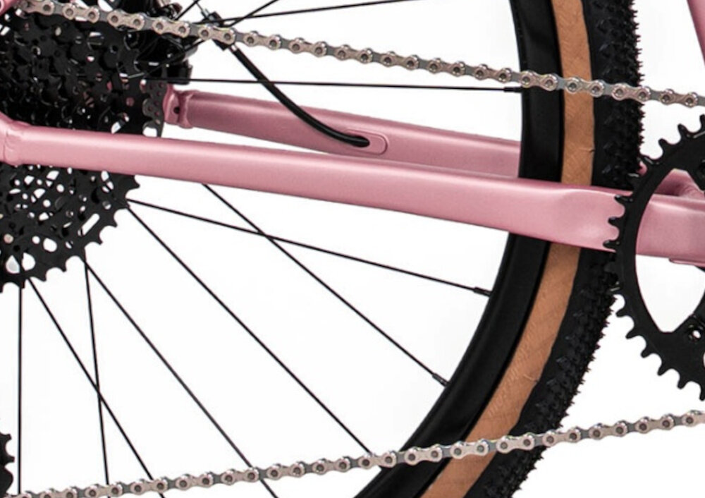Rower gravel ROMET Aspre 2.1 U18 28 cali Różowy zbliżenie na łańcuch białe tło stalowy łańcuch marki ROMET konstrukcja ogniw wspiera płynną współpracę z kasetą i zębatkami bardziej równomierne przenoszenie mocy mniejsze zużycie pozostałych elementów napędu