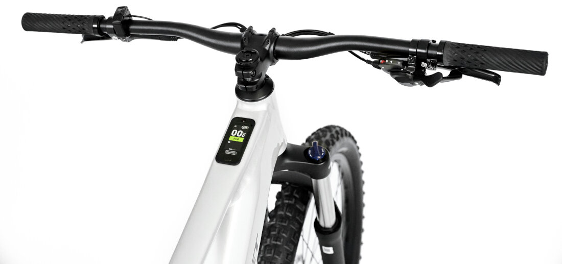 Rower elektryczny ROMET E-Mustang 1.0 U17 28 cali Srebrny Zbliżenie na wyświetlacz roweru elektrycznego z widocznym odczytem \'0.0 km/h\'. Obok wyświetlacza znajdują się przyciski z oznaczeniami \'+\' i \'-\'.