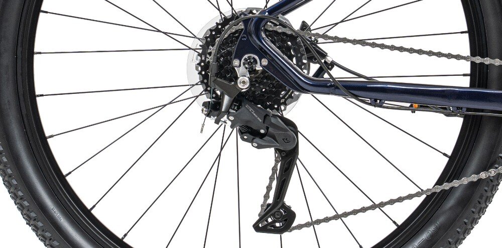 Zdjęcie przedstawia tylne koło roweru górskiego z widocznym mechanizmem przerzutki i łańcuchem. Rama roweru jest w kolorze granatowym.