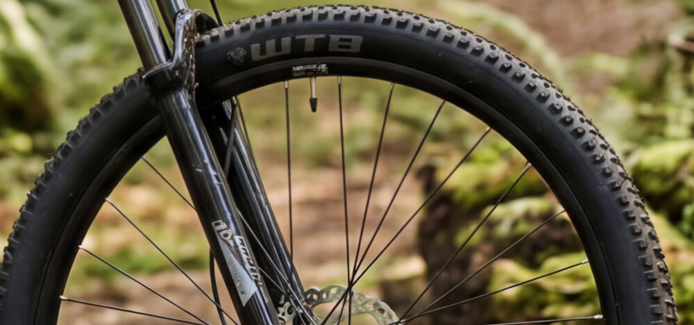 Rower górski MTB ROMET Mustang 4.1 U20 29 cali Zielony rozmazane tło zbliżenie na oponę widok z boku marki WTB w rozmiarze 29 cali głęboki bieżnik skutecznie wspiera jazdę utrzymanie stabilnego toru jazdy obręcze WTB ST o szerokości 30 mm stabilność piasty SHIMANO HB-TC500-B 15x110 mm z przodu piasty SHIMANO FH-TC500-B 12x148 mm z tyłu regularne sprawdzanie ciśnienia powietrza wartość na bocznej części opony