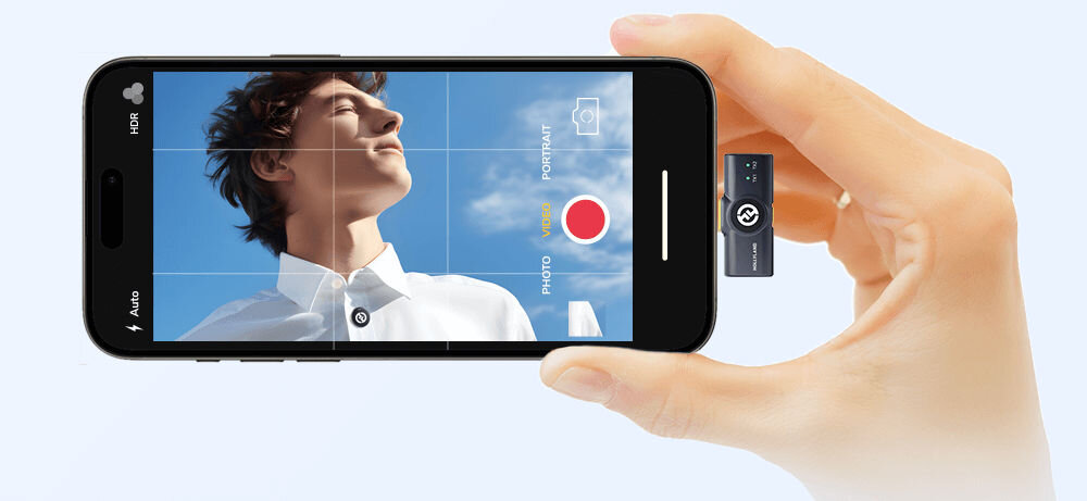 System bezprzewodowy HOLLYLAND Lark M2 Lightning Grafitowy prezentacja odbiornika podłączonego do telefonu włączone nagrywanie ręka trzymająca telefon pastelowe tło w odcieniach fioletu odsłuchiwanie nagrania bez odłączania odbiornika skrócenie czasu pracy weryfikacja