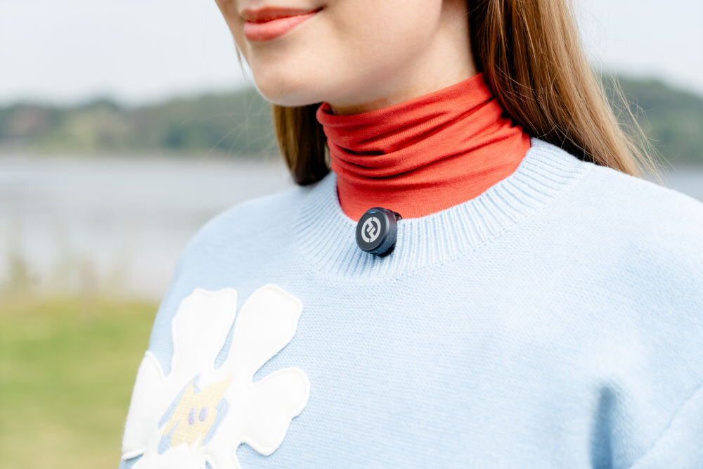 System bezprzewodowy HOLLYLAND Lark M2 Lightning Grafitowy prezentacja mikrofonu przyczepionego do swetra dziewczyny w tle zieleń algorytmy obróbki dźwięku czyste brzmienie ograniczenie zakłóceń