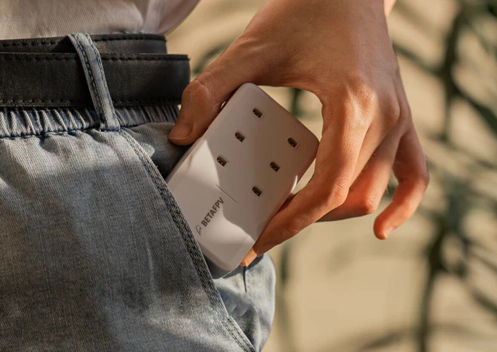 Ładowarka BETAFPV 6 Port 1S Osoba wsuwająca białą, kompaktową ładowarkę do przedniej kieszeni jeansowych spodni, trzymając urządzenie w prawej dłoni