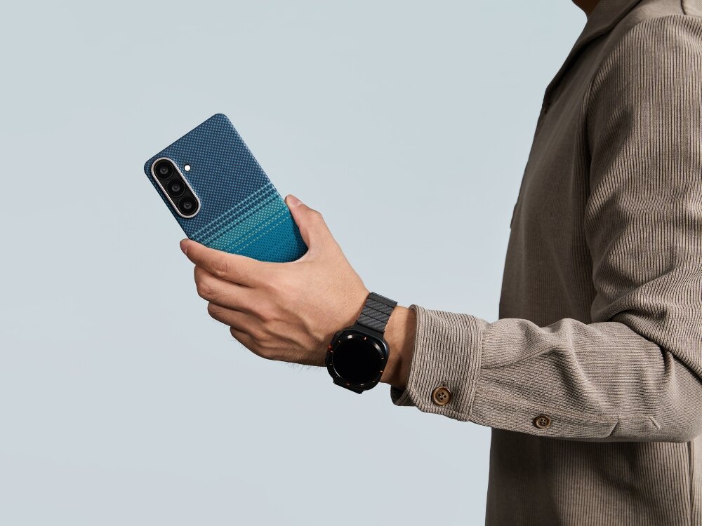 Etui PITAKA Ultra-Slim MagSafe Samsung Galaxy S26 - włókno aramidowe, smukłe, MagSafe Smartfon Mężczyzna trzymający smartfon w etui Pitaka o wzorze aramidowym, prezentujący dopasowany pasek do zegarka typu smartwatch.