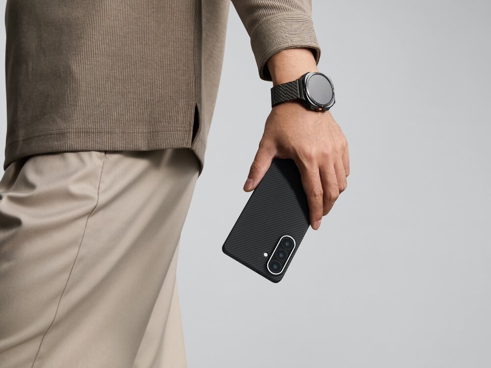 Etui PITAKA Ultra-Slim MagSafe Samsung Galaxy S26 - wytrzymałe włókno, nowoczesny splot Mężczyzna trzymający smartfon Samsung Galaxy S24 w etui Pitaka z włókna aramidowego, widoczny pasujący pasek do zegarka.