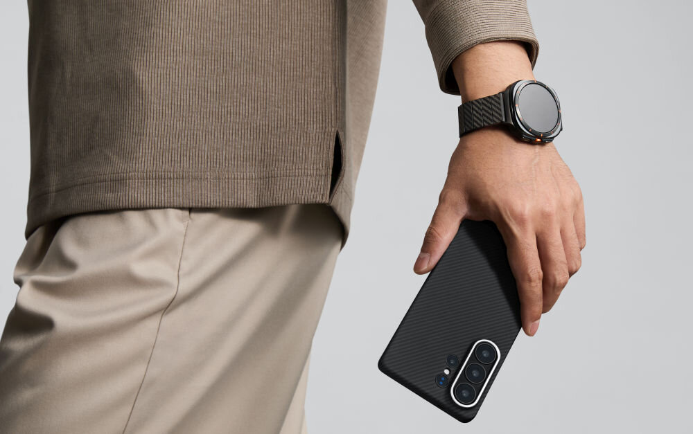 Etui PITAKA Ultra-Slim MagSafe Samsung Galaxy S26 - wytrzymałe włókno, nowoczesny splot Mężczyzna trzymający smartfon Samsung Galaxy S24 w etui Pitaka z włókna aramidowego, widoczny pasujący pasek do zegarka.