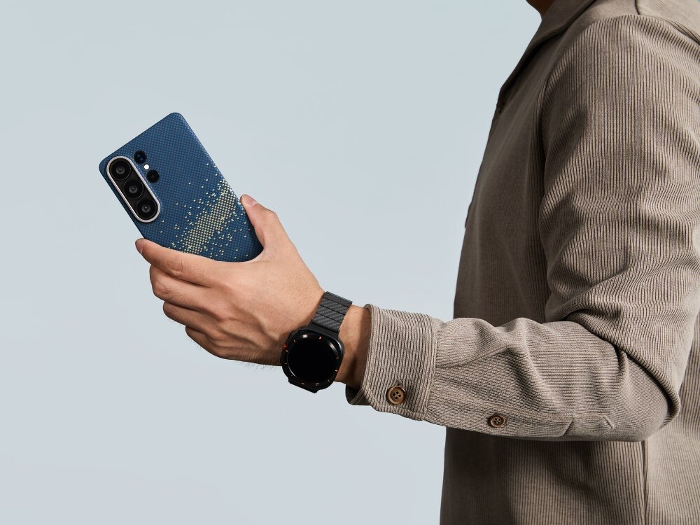 Etui PITAKA Ultra-Slim MagSafe Samsung Galaxy S26 - włókno aramidowe, smukłe, MagSafe Smartfon Mężczyzna trzymający smartfon w etui Pitaka o wzorze aramidowym, prezentujący dopasowany pasek do zegarka typu smartwatch.