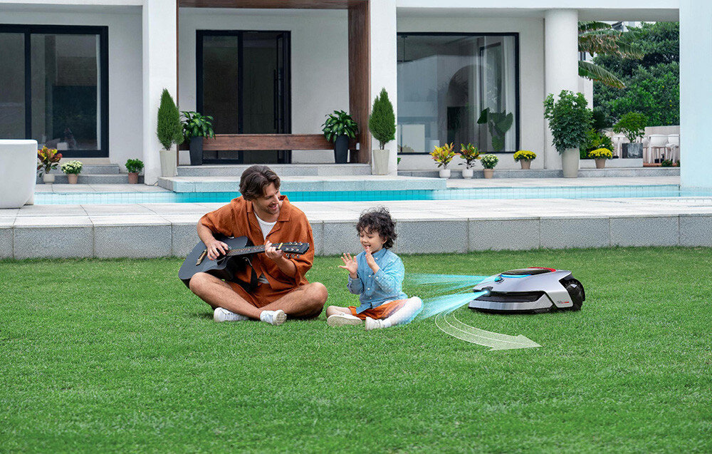 Robot koszący DREAME A2 robot na trawie obok dziecko i dorosła osoba grająca na gitarze osoby siedzą na trawniku w tle dom z basenem zaawansowany robot koszący innowacyjne technologie intuicyjne rozwiązania funkcje OmniSense™ 2.0 i EdgeMaster™ Cutting System praca na terenie z nachyleniami do 50% do trawników o powierzchni do 3000 m²