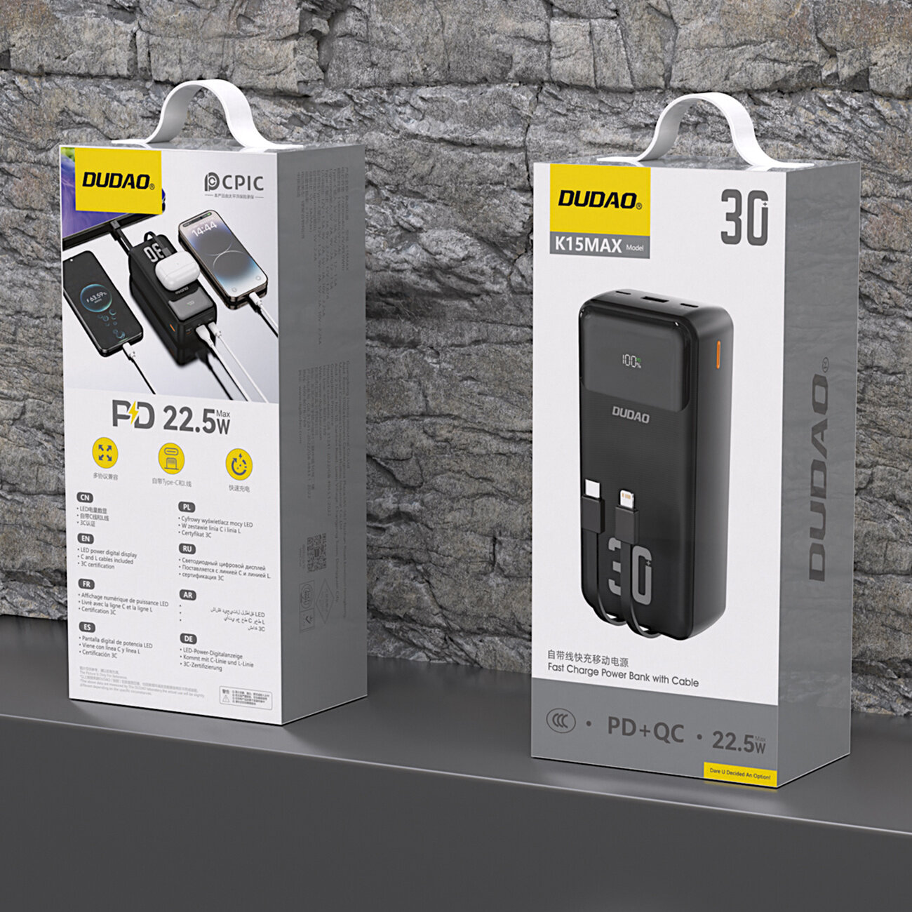 Na obrazie widoczne są dwa opakowania produktu marki DUDAO. Na jednym z nich znajduje się czarny powerbank z wbudowanymi kablami, a na drugim przedstawiono jego funkcje i specyfikacje, takie jak PD 22.5W.