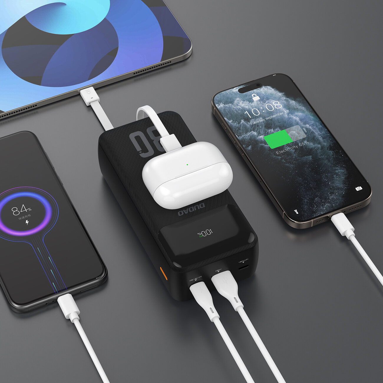 Na obrazie widoczny jest czarny powerbank z wbudowanymi kablami, do którego podłączone są trzy urządzenia: dwa smartfony i etui na słuchawki. Na wyświetlaczu powerbanka widoczny jest napis \'00\'.