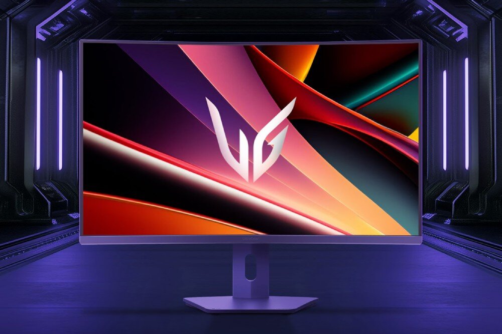 Monitor z kolorowym, abstrakcyjnym wzorem na ekranie, z widocznym logo \'UG\'. Tło jest ciemne z fioletowymi światłami po bokach.