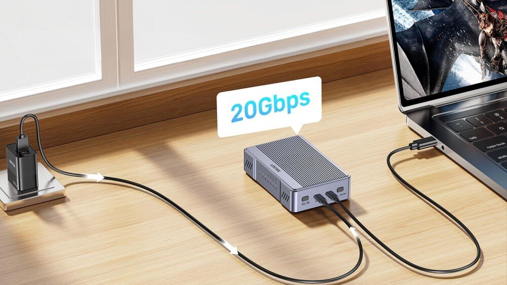 Na drewnianym blacie znajduje się obudowa dysku podłączona do laptopa i zasilacza. Nad obudową widoczny jest napis \'20Gbps\'.