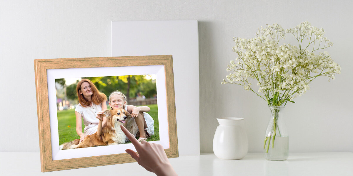 Ramka cyfrowa KODAK RCF-1012W Brązowy DOTYK Palec wskazujący dotykający ramkę, w tle doniczka z rośliną