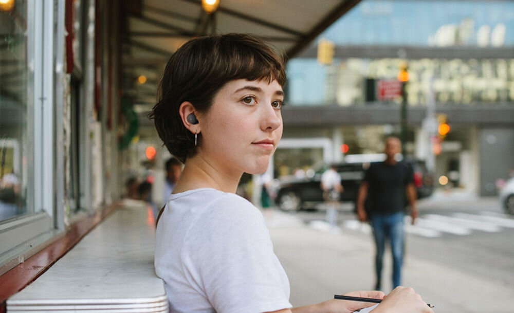 Słuchawki dokanałowe JBL Wave Buds 2 z dynamicznym brzmieniem Pure Bass, osoba z założonymi słuchawkami siedząca na ławce w plenerze