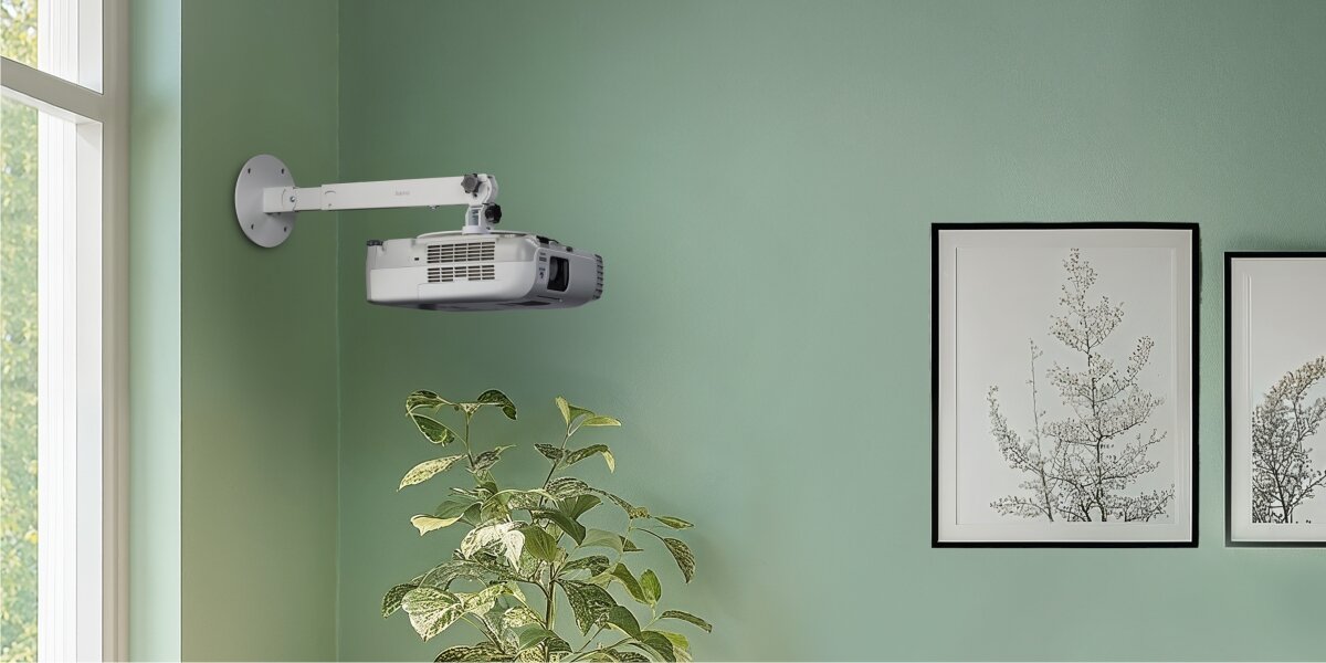 Uchwyt sufitowo-ścienny HAMA 220880 Maksymalne obciążenie 15 kg Biały Projektor multimedialny zainstalowany na białym uchwycie ściennym w salonie o zielonych ścianach obok dekoracyjnych obrazów.